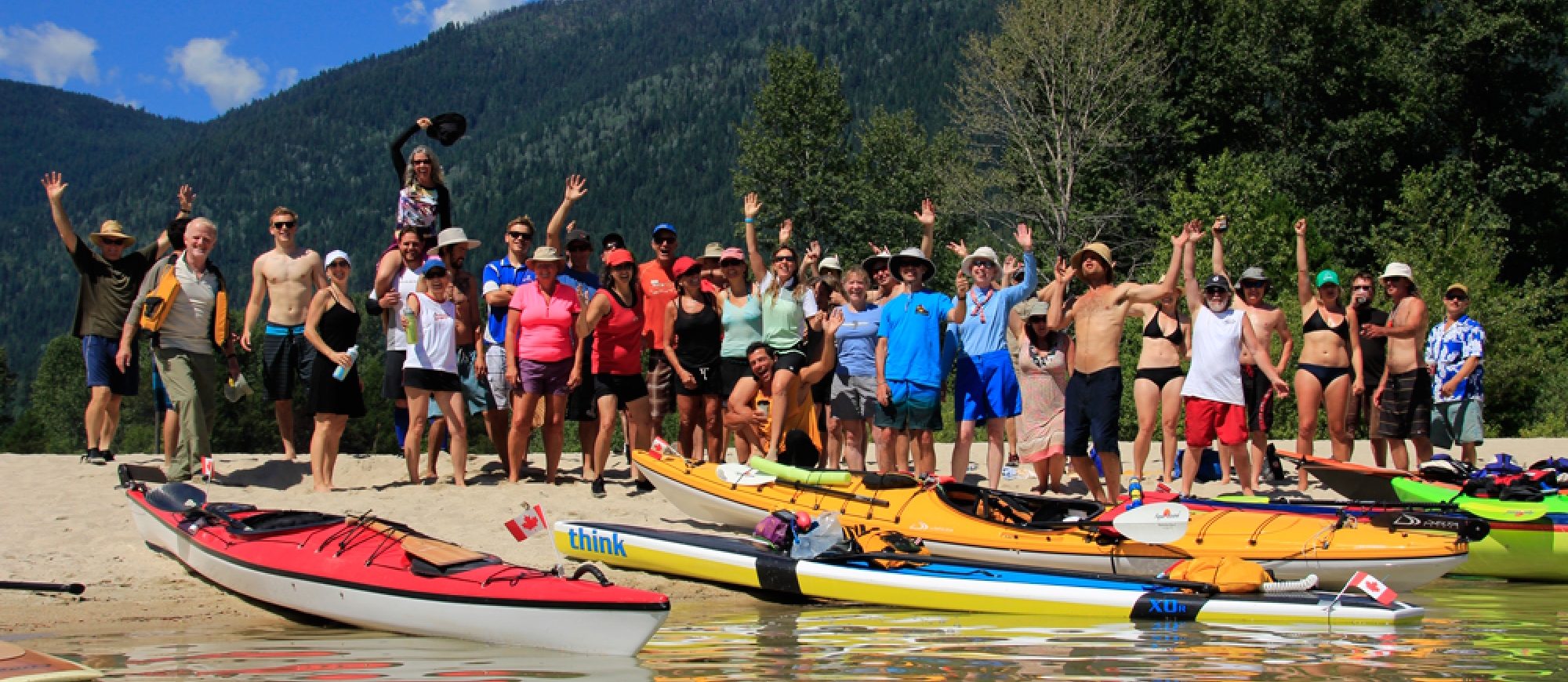 A large group of paddlers standing on the beach waving at Kokanee Creek Provincial Park